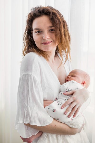 portrait-smiling-mother-carrying-her-baby-front-white-curtain